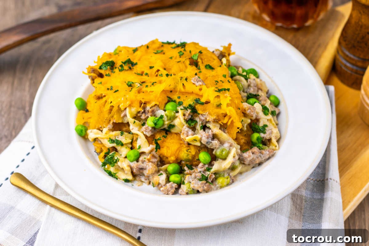 A close-up of a serving of Amish Country Casserole, showcasing the perfectly cooked ground beef, vibrant green peas, and wide egg noodles coated in a rich, creamy sauce, all topped with beautifully melted golden cheese.