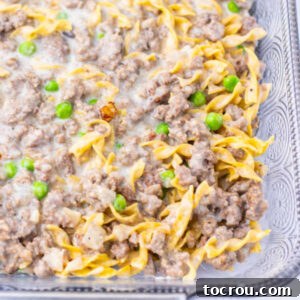 Baking dish with creamy mixture of egg noodles, peas, and ground beef ready to get covered with foil and go in the oven.