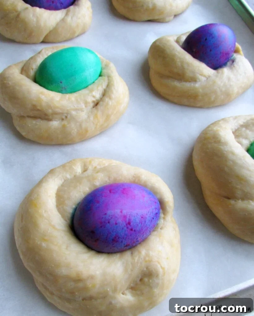 small proofed easter bread doughs with colored eggs in the center.