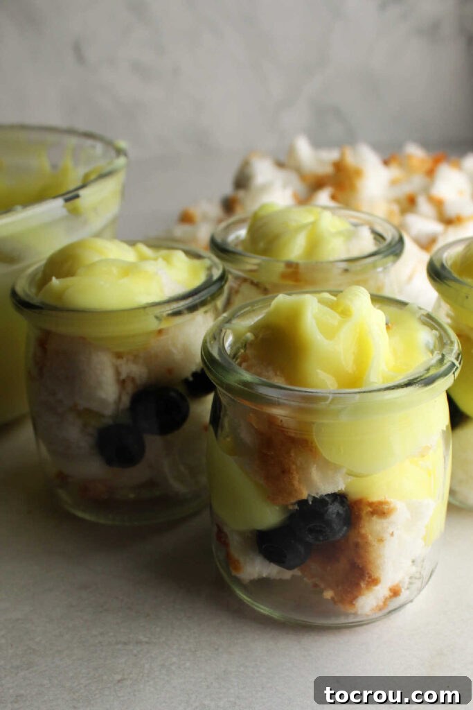 Zesty Lemon Blueberry Parfaits 3 Layering angel food cake cubes, lemon mixture, and blueberries in small glass jars for individual parfaits.