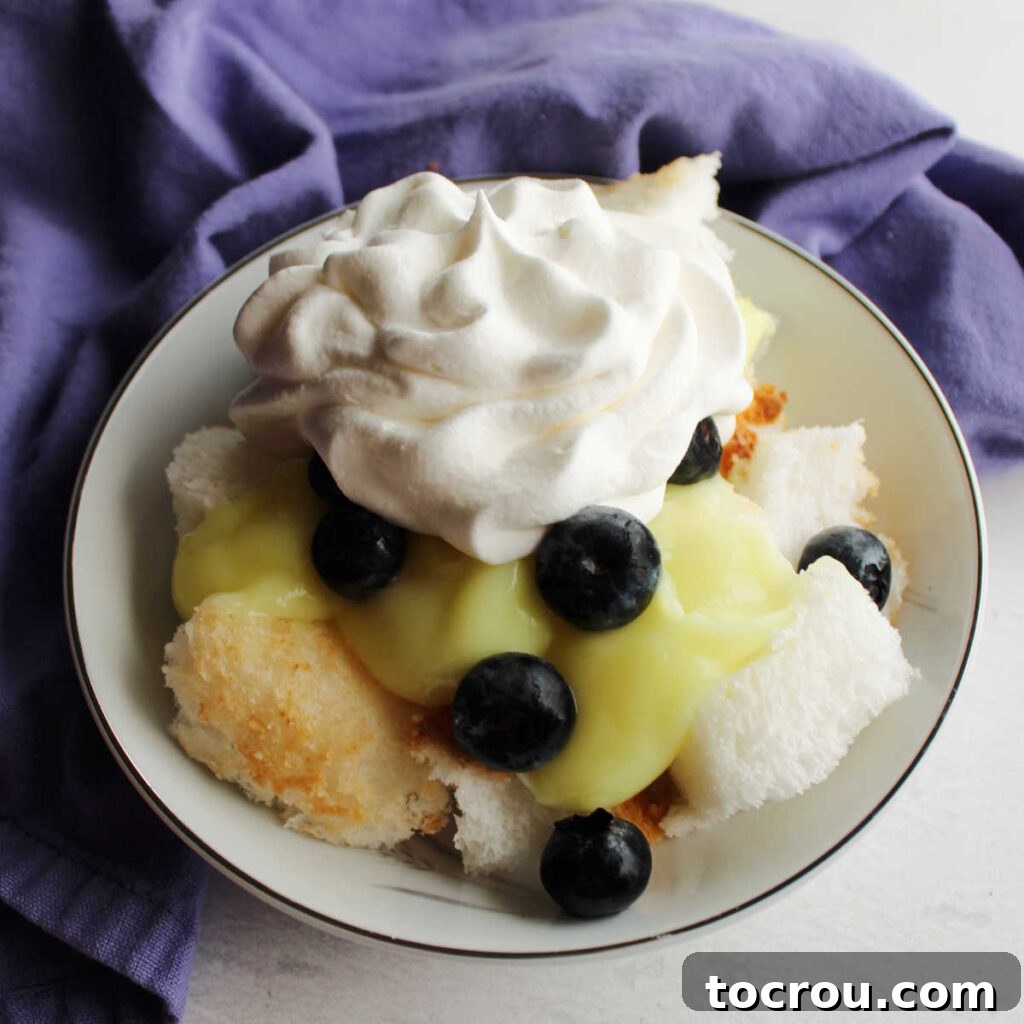 Zesty Lemon Blueberry Parfaits 5 Close-up of a small bowl filled with lemon blueberry trifle, showcasing layers of cake, creamy lemon filling, and vibrant blueberries with whipped topping.