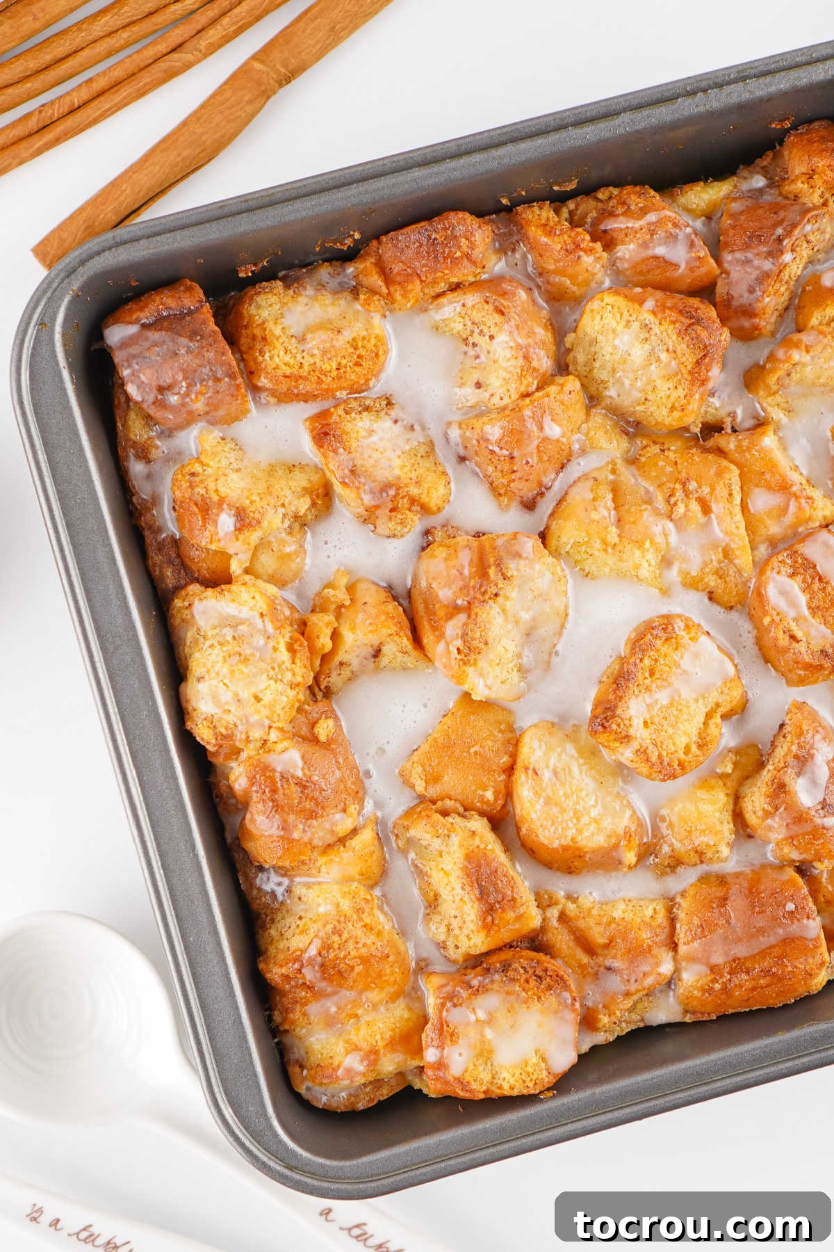 A square baking dish filled with freshly baked donut bread pudding, beautifully topped with a delicate powdered sugar glaze, ready for serving.