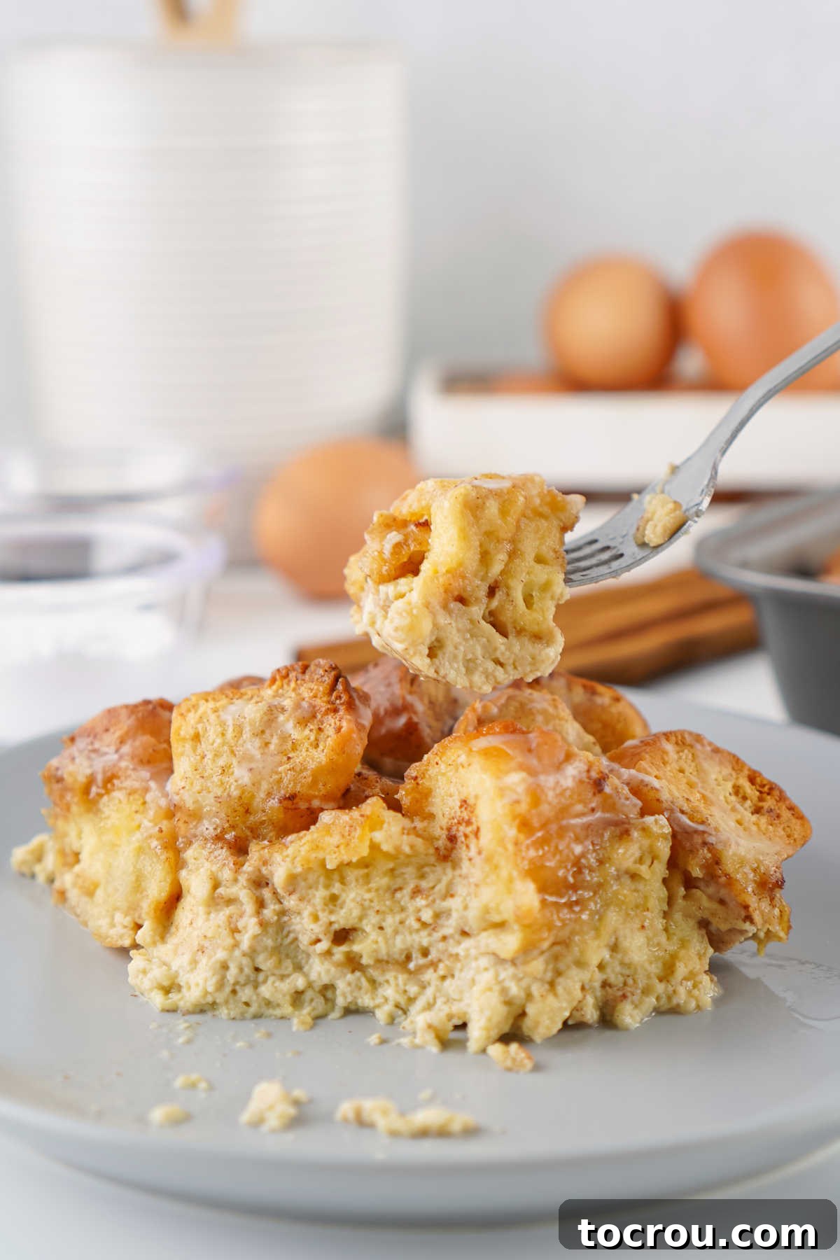 A fork holding a bite-sized piece of donut bread pudding, ready to be eaten, showcasing its moist texture and sugary topping.