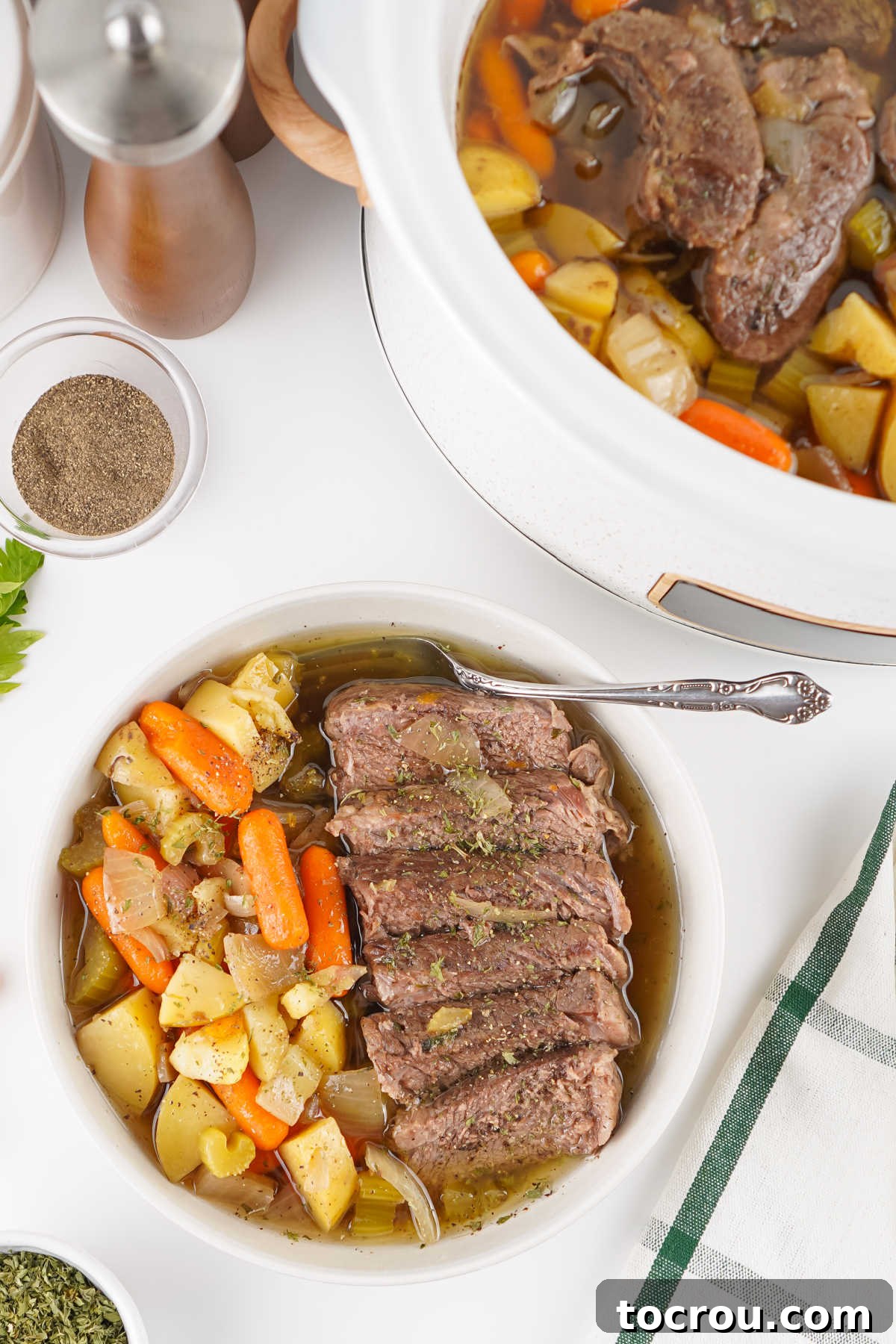 Plate of pot roast with slices of roast beef with veggies in a light beef gravy.