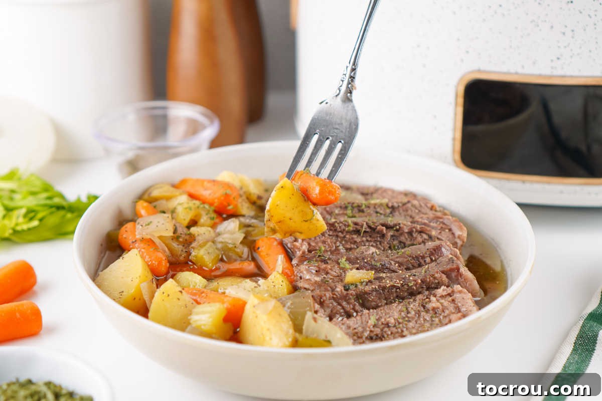 Fork getting some potatoes and carrots from a bowl of pot roast.