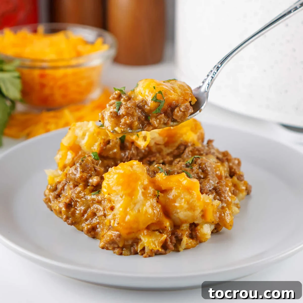 Fork with a bite of taco tater tot casserole on it showing cheesy seasoned beef mixture with golden tater tots with melted cheese on top.