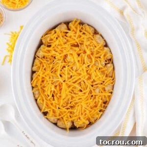 Tater tots and shredded cheese over the top of the cheesy taco meat mixture in a crockpot, ready to cook.