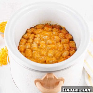 Finished tater tot casserole in slow cooker with golden brown tater tots and melted cheese on top.