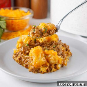 Fork with a bite of taco tater tot casserole on it showing cheesy seasoned beef mixture with golden tater tots with melted cheese on top.