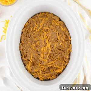 Meat and cheese mixture spread over the top of some tater tots in a slow cooker.