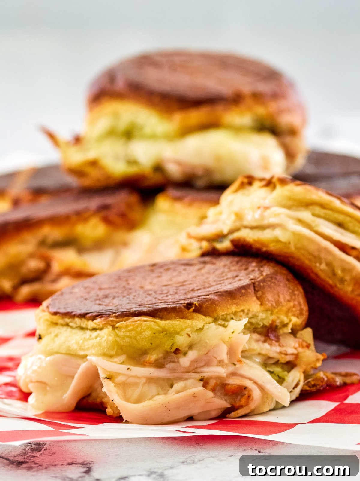 A close-up view of a turkey grilled cheese slider revealing layers of vibrant pesto and sweet dried cranberries nestled within melted cheese.