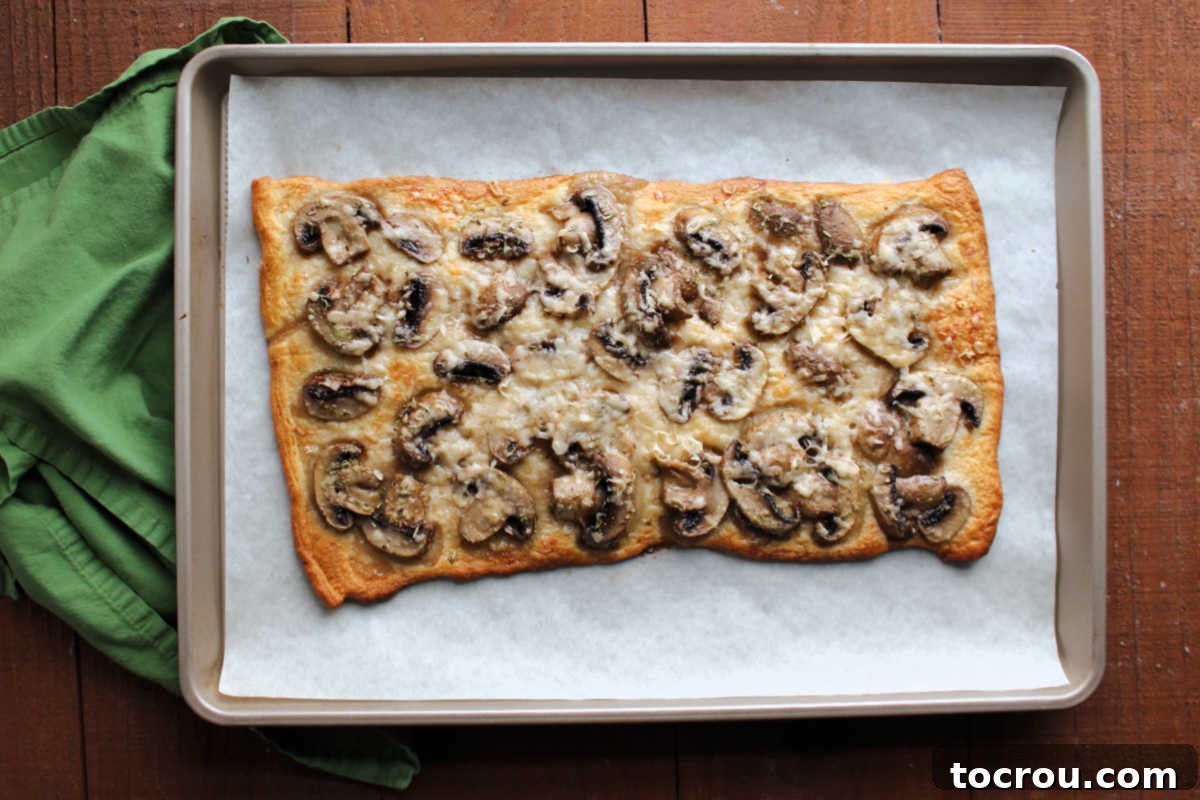 Freshly baked mushroom flatbread, perfectly golden and aromatic, cooling on a parchment paper-lined baking tray, ready to be sliced and served as a delightful appetizer.