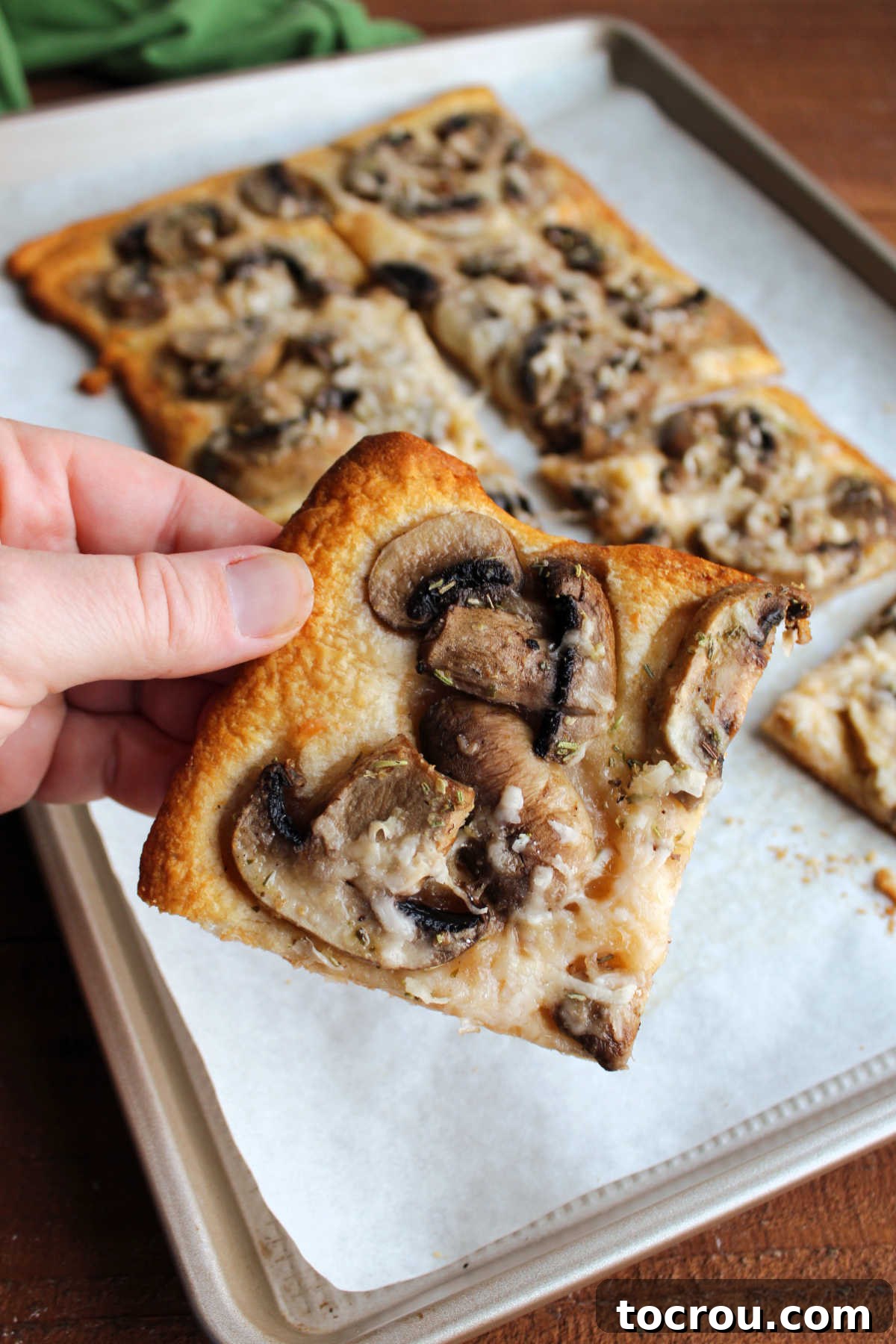A hand gently holding a warm piece of mushroom flatbread, showcasing the golden crescent crust, melted garlic butter, and savory Parmesan cheese, ready for a delicious bite.