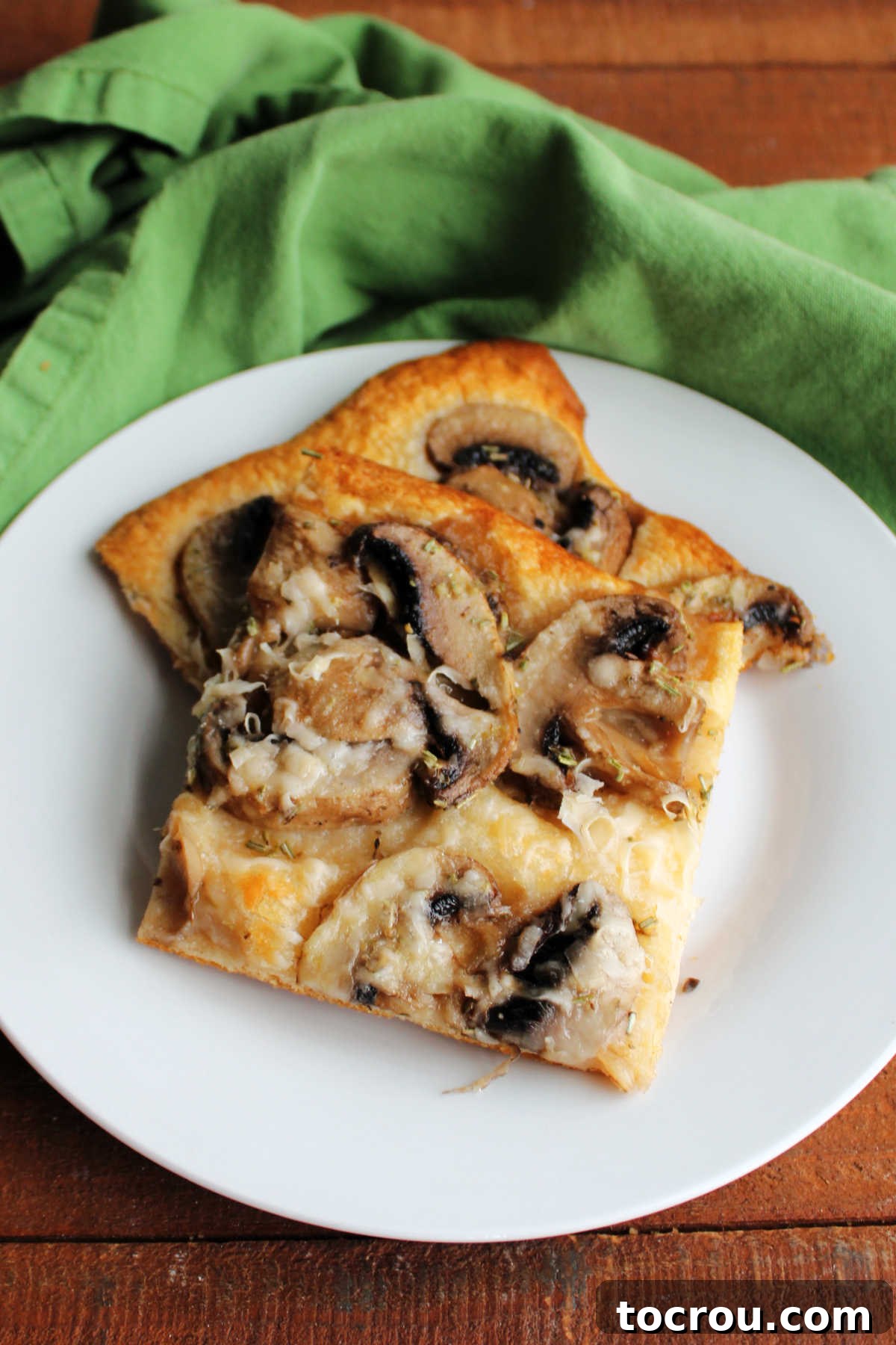 A simple white plate featuring two inviting pieces of mushroom flatbread, beautifully presented and ready to be enjoyed as a delightful snack or appetizer.