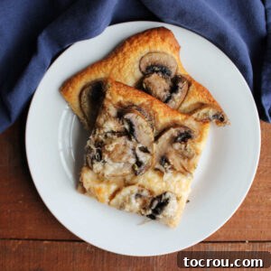 Two pieces of mushroom flatbread with slices of mushrooms in garlic butter with rosemary and Parmesan cheese on golden crescent roll crust.