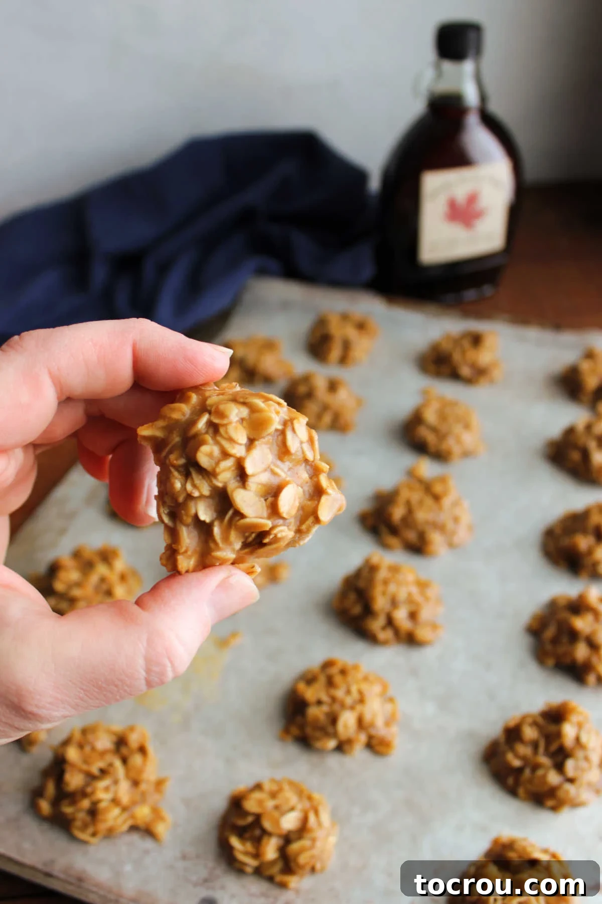 Easy Maple No-Bake Treats 5 Hand holding a no bake maple cookie over a tray with more cookies that have been scooped on wax paper to set.