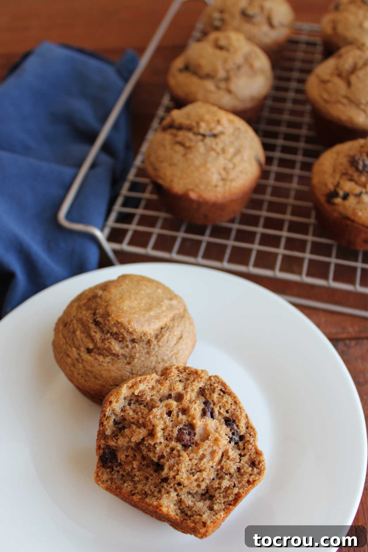 One and a half bran muffins are arranged on a small plate, with the cut muffin revealing its soft, airy texture dotted generously with plump raisins and the distinctive tan color of bran throughout its interior. It looks moist and wholesome.