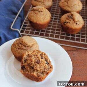 Half of a bran muffin on a plate showing its airy interior dotted with raisins with more freshly baked homemade bran muffins in the background.
