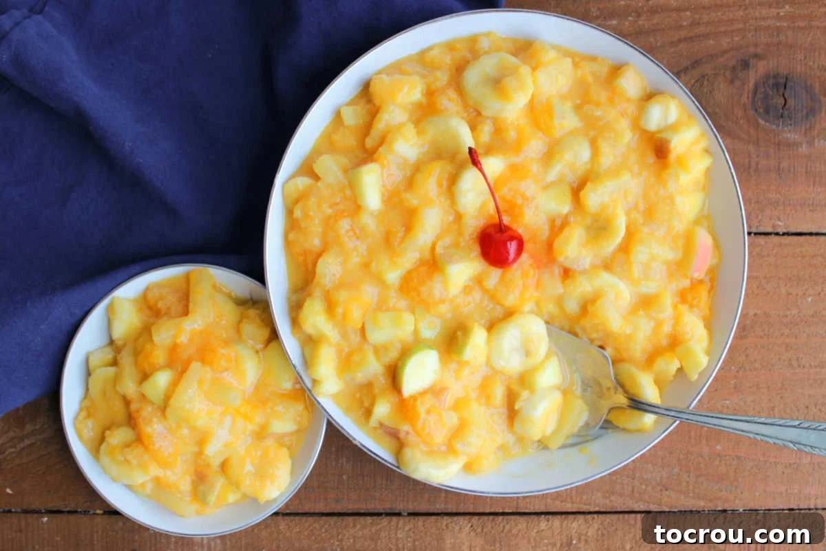 Zesty Fruit Medley 2 Large serving bowl of Tang fruit salad topped with a maraschino cherry next to a smaller bowl with a serving of fruit salad in creamy orange dressing, ready to eat.