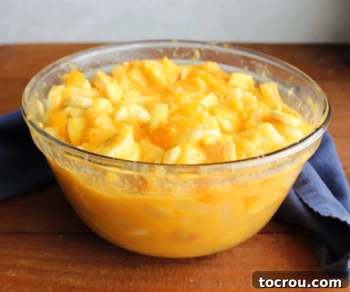 Zesty Fruit Medley 4 Mixing bowl filled with fruit coated in creamy orange Tang dressing, ready to be chilled.