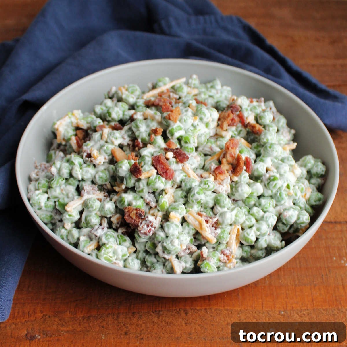 Serving bowl filled with creamy pea salad with creamy dressing, cheese and crumbled bacon.