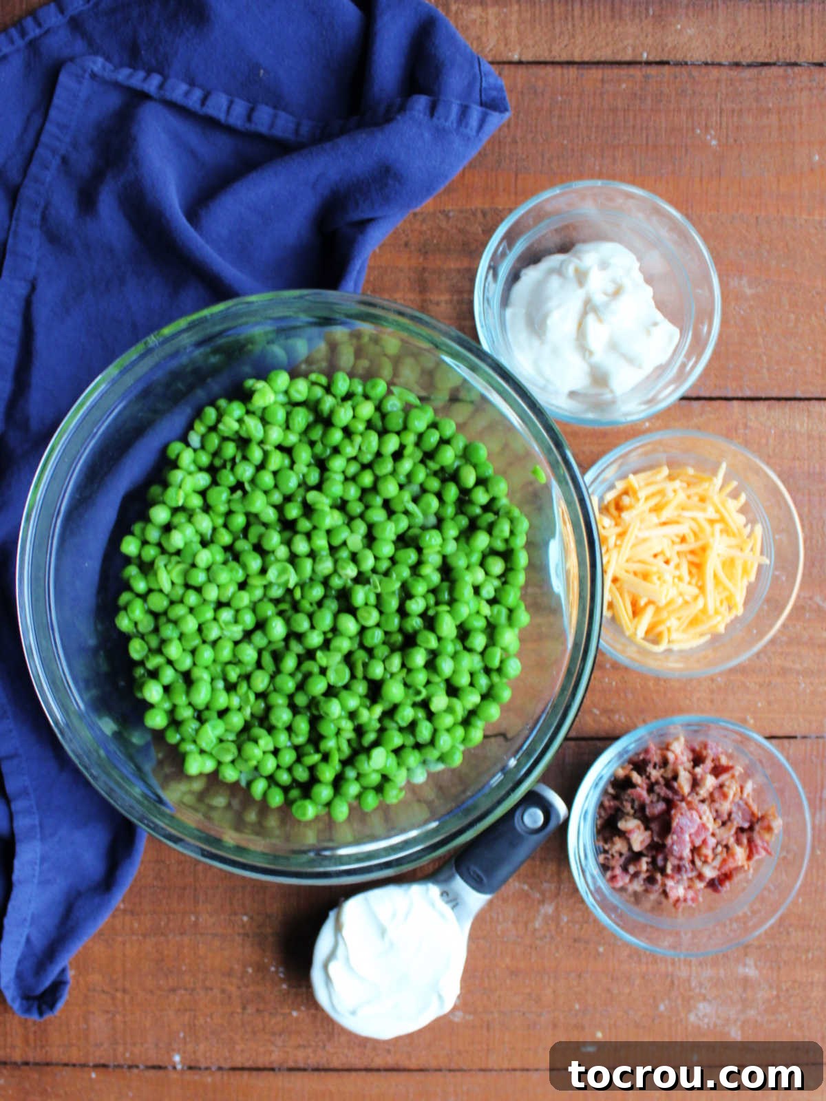 Ingredients including peas, sour cream, miracle whip, shredded cheddar and crumbled bacon ready to be made into a pea salad.