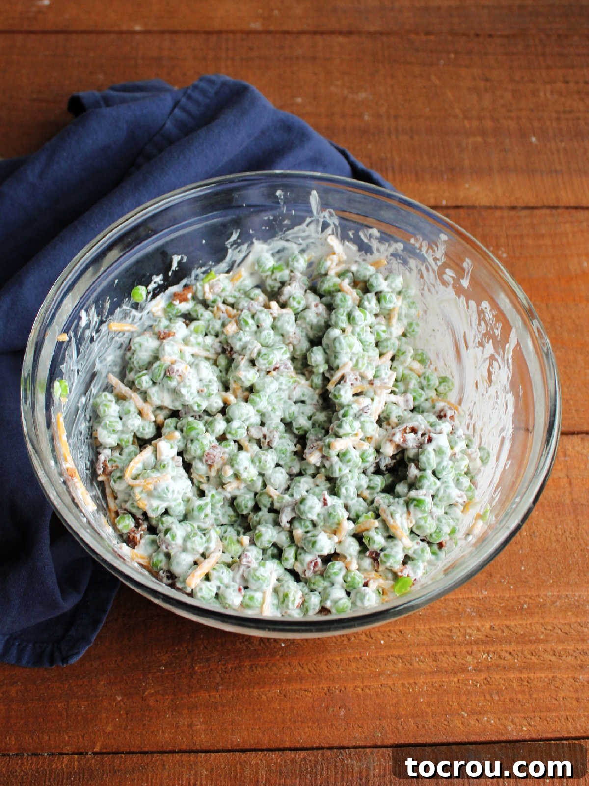 Mixing bowl filled with pea salad with bacon and cheese, ready to chill in the fridge.