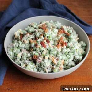 Serving bowl filled with creamy pea salad with creamy dressing, cheese and crumbled bacon.
