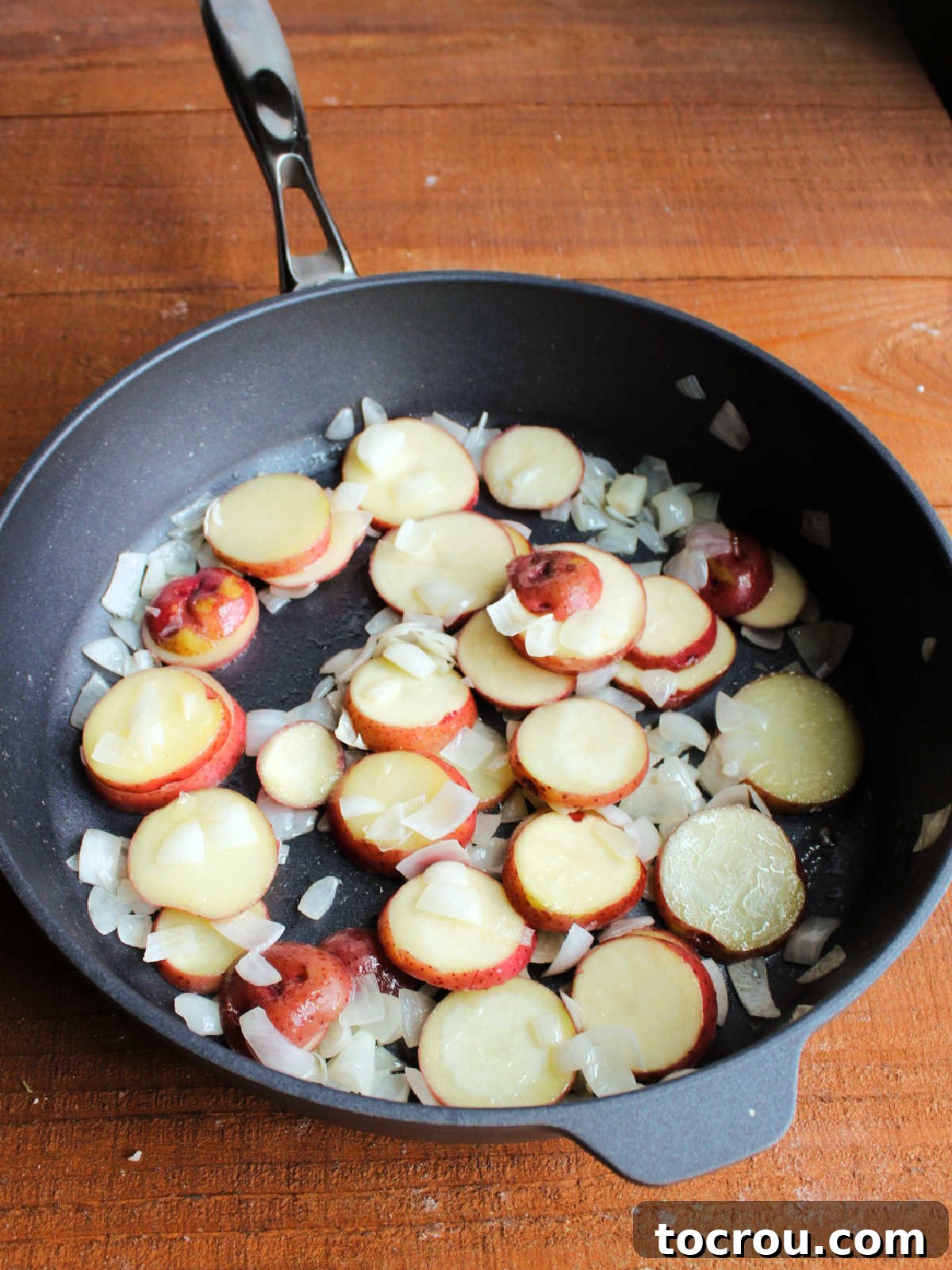 Large skillet with diced onions and sliced peppers cooked in butter.
