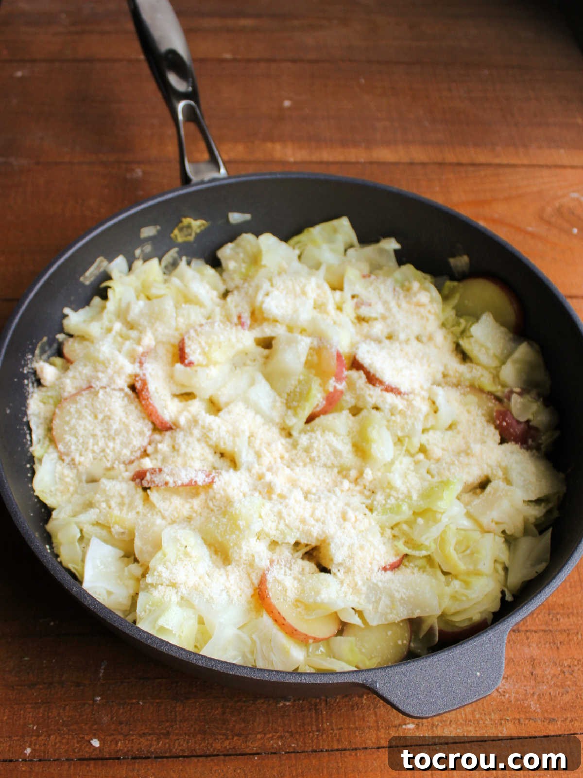 Skillet filled with cooked cabbage and potatoes topped with grated Parmesan cheese.