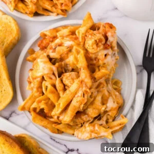 Dinner plate piled high with penne pasta coated in tomato sauce, with chunks of chicken and melted cheese, ready to eat. A satisfying meal that's easy to prepare.