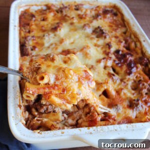 spoon lifting serving of baked ziti out of pan. A perfectly golden and bubbly baked ziti, ready to be served.