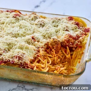 Casserole dish filled with baked spaghetti and meatballs casserole with one serving missing showing the cheesy pasta, sauce, and meatballs inside. A hearty and satisfying spaghetti bake.