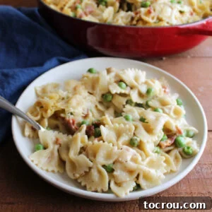 Plate of baked pasta with alfredo sauce, peas, and bacon, ready to eat. A creamy and savory alfredo pasta dish.