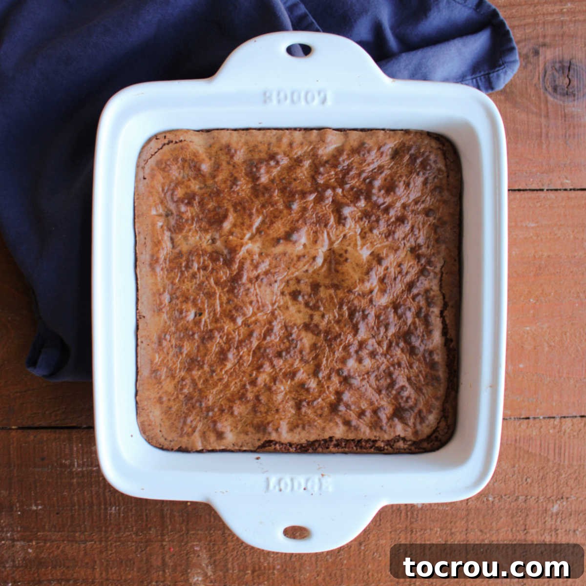 Square baking dish with batch of freshly baked prune brownies inside, their surfaces crinkled and glistening, ready to be cut and served.