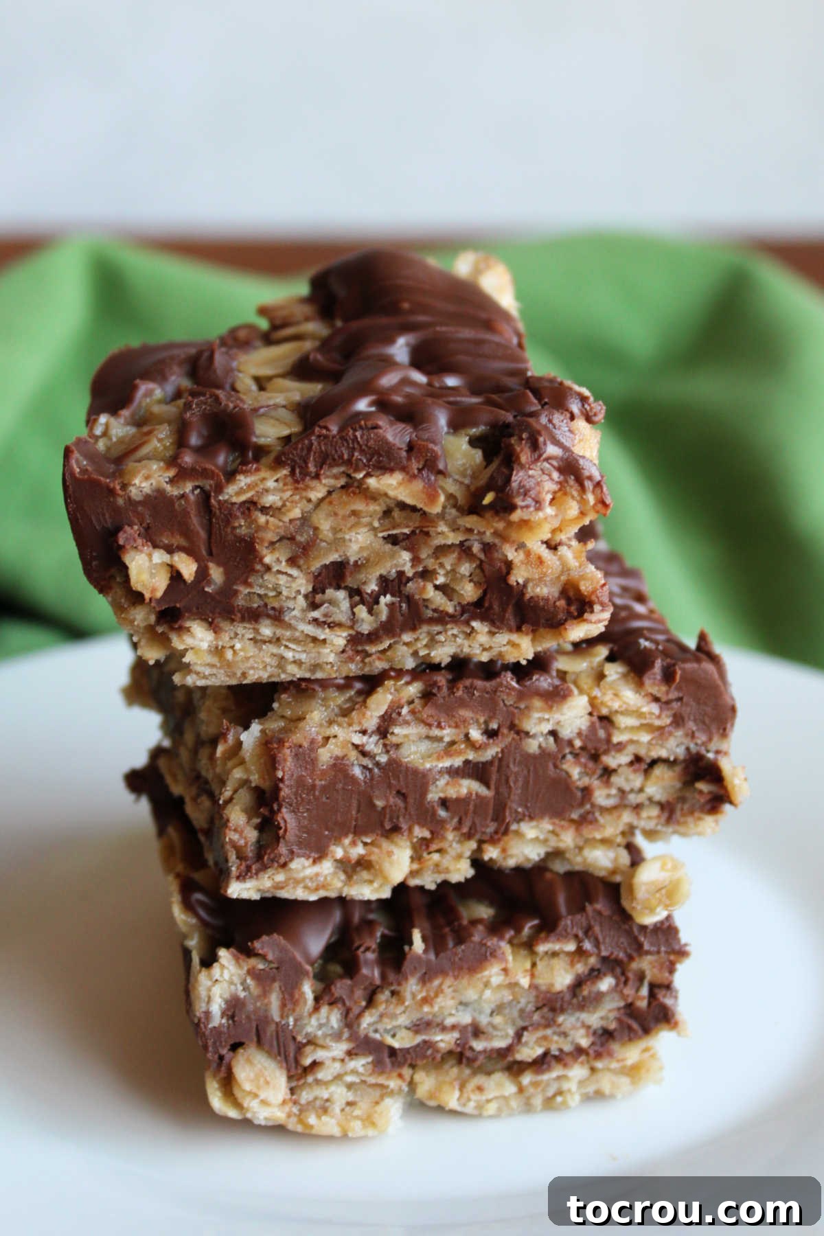 Close-up shot of no-bake oatmeal cookie bars, neatly stacked to highlight the distinct layers of the oat base and the rich chocolate peanut butter filling, set against a rustic background.