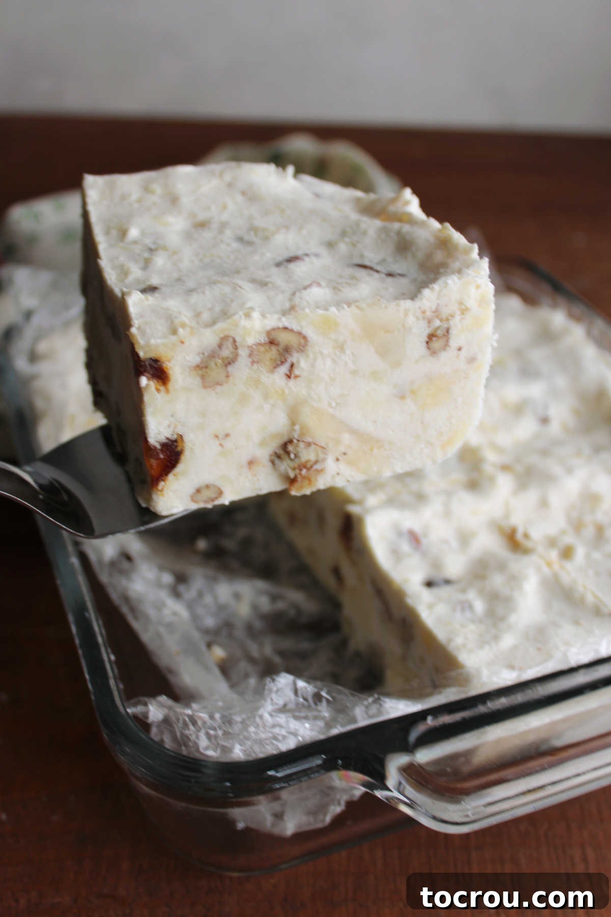 Spatula lifting a piece of frozen date and cheese salad out of the glass baking dish that it was frozen in. 