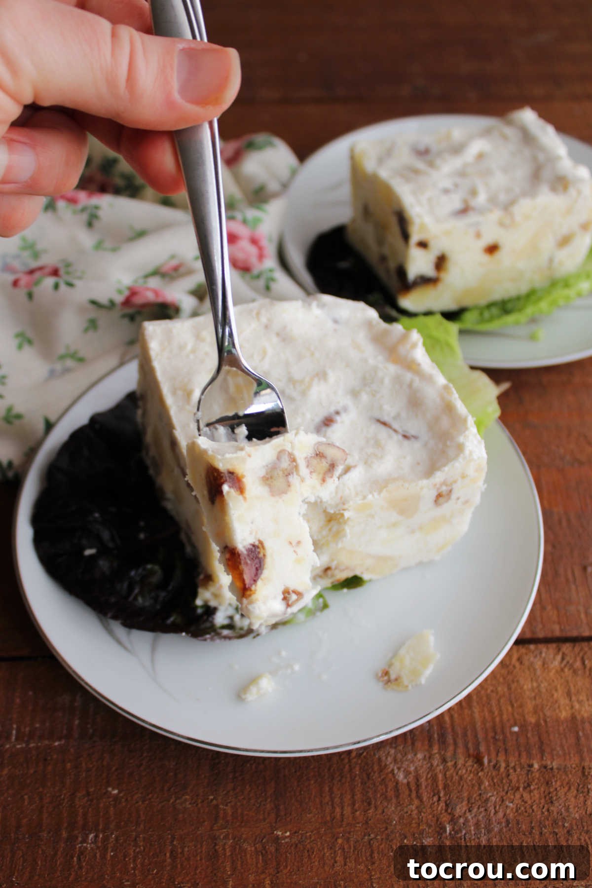 Bite of frozen date and cream cheese salad on fork showing bits of fruits and nuts frozen in a creamy base. 