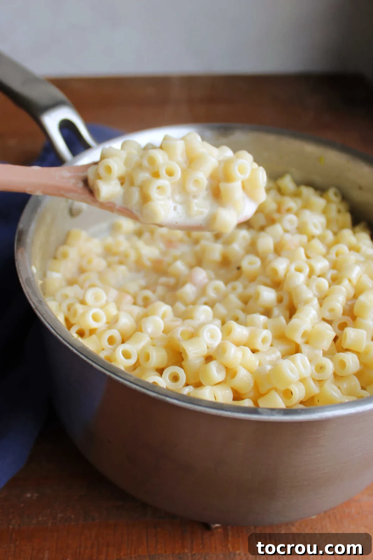 A spoon getting a generous scoop of creamy one-pot ditalini pasta, adorned with flakes of Parmesan and freshly ground black pepper, directly from the saucepan.