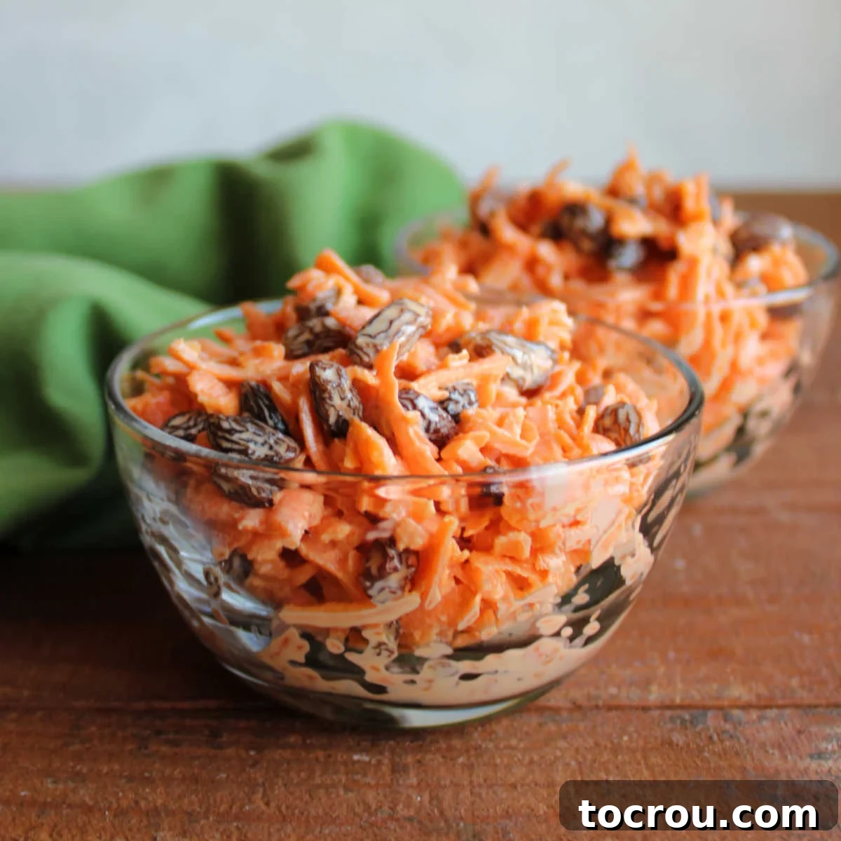 Heirloom Carrot Raisin Salad 2 Two small bowls filled with a vibrant salad made from finely shredded carrots and plump raisins, all coated in a light, creamy orange-infused dressing.