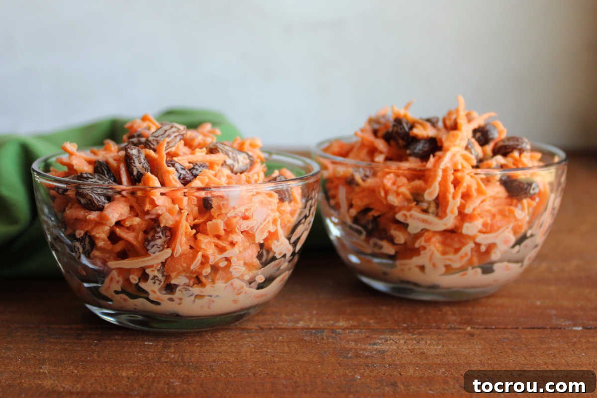 Heirloom Carrot Raisin Salad 4 Two elegant small glass bowls, each generously filled with a serving of carrot raisin salad, showcasing the delightful combination of shredded carrots and plump raisins bathed in a smooth, creamy Tang-infused dressing.