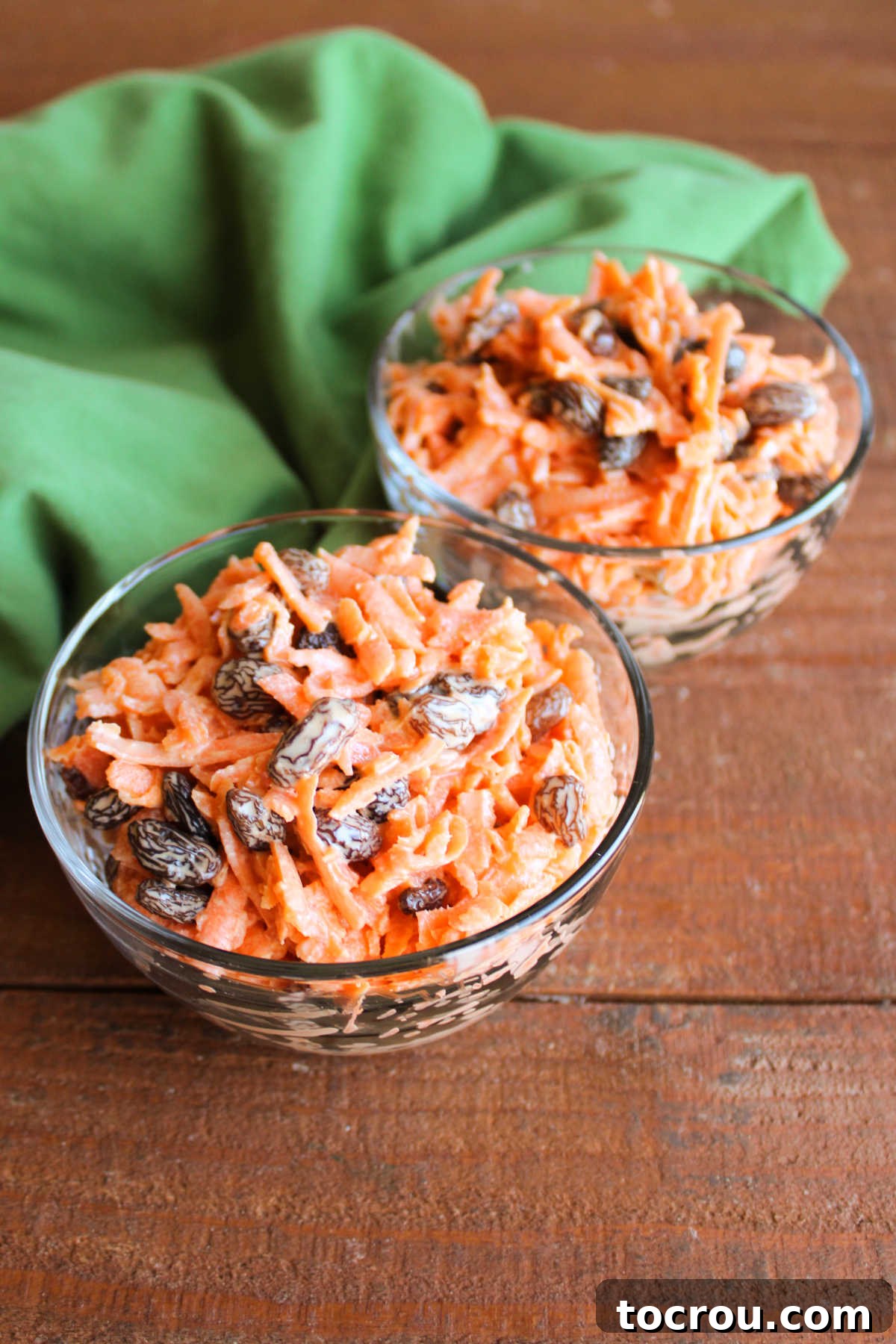 Heirloom Carrot Raisin Salad 5 An overhead view of two glass bowls filled with carrot raisin salad, showing the finely shredded carrots and plump raisins generously coated in the creamy, orange-tinted dressing, ready for serving.