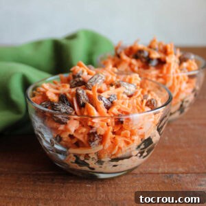 Two small bowls filled with a vibrant salad made from finely shredded carrots and plump raisins, all coated in a light, creamy orange-infused dressing.