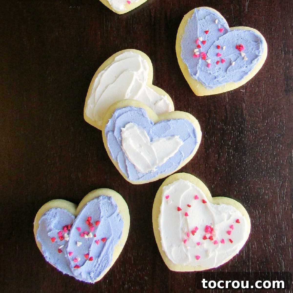 Sour cream cookies cut in the shape of hearts topped with buttercream frosting and sprinkles.