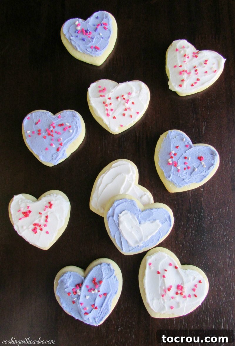 Heart shaped sour cream cookies with white and lavender buttercream and sprinkles on top.