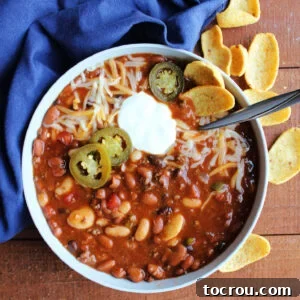 Bowl of venison chili with lots of beans topped with shredded cheese, jalapenos and a dollop of sour cream, making a satisfying meal for cold weather.