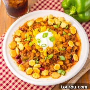 Bowl filled with copycat Wendy's chili topped with cheese, oyster crackers, sour cream, and green onions, ready to eat for a classic chili dinner.