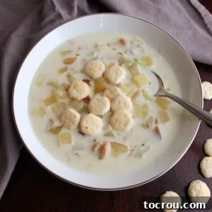 Close up of spoon in bowl of creamy New England clam chowder with oyster crackers, ready to enjoy a comforting seafood meal for dinner.