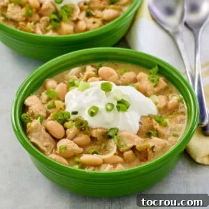 Bowl of creamy white chicken chili with white beans and green chilies topped with sour cream and green onions, ready for a comforting dinner.