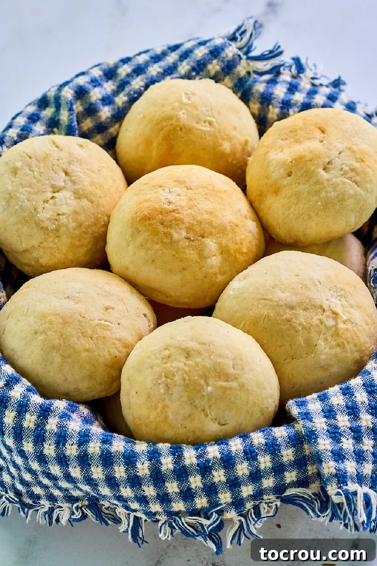 Basket lined with blue and white checked towel and filled with soft golden brown potato rolls.
